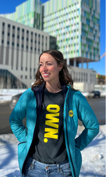 A mid-thirties woman smiling and standing outside a cancer centre.