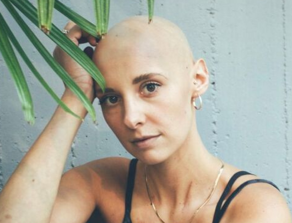 Photo of cancer patient with no hair in jeans and tank top posing for portrait