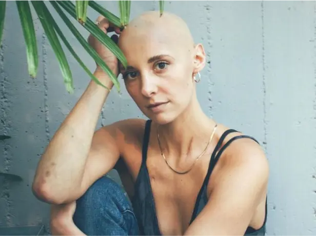 Photo of cancer patient with no hair in jeans and tank top posing for portrait