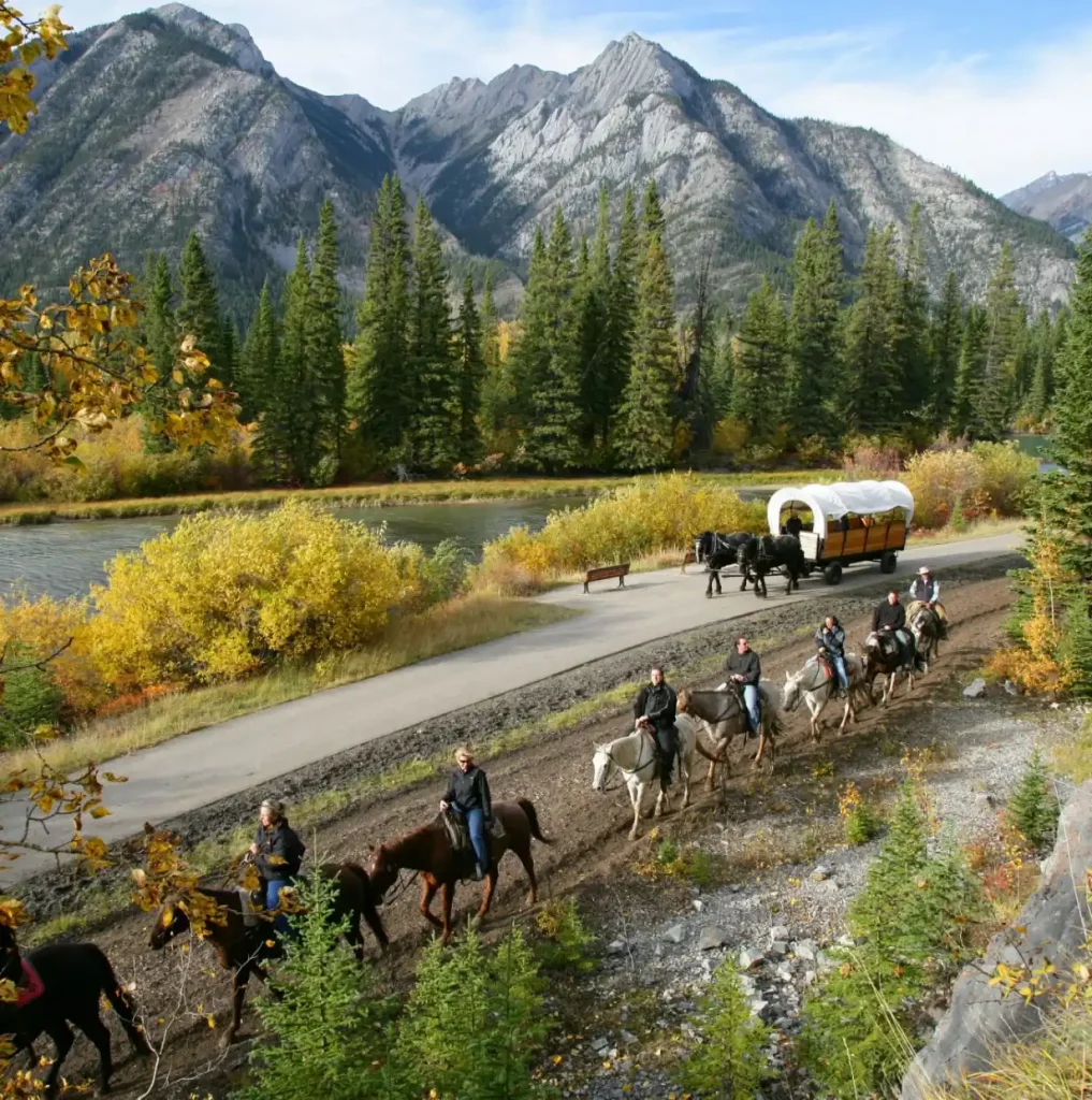 scenic view of the Rocky Mountains and the Bow River with a wagon ride and people on horse back