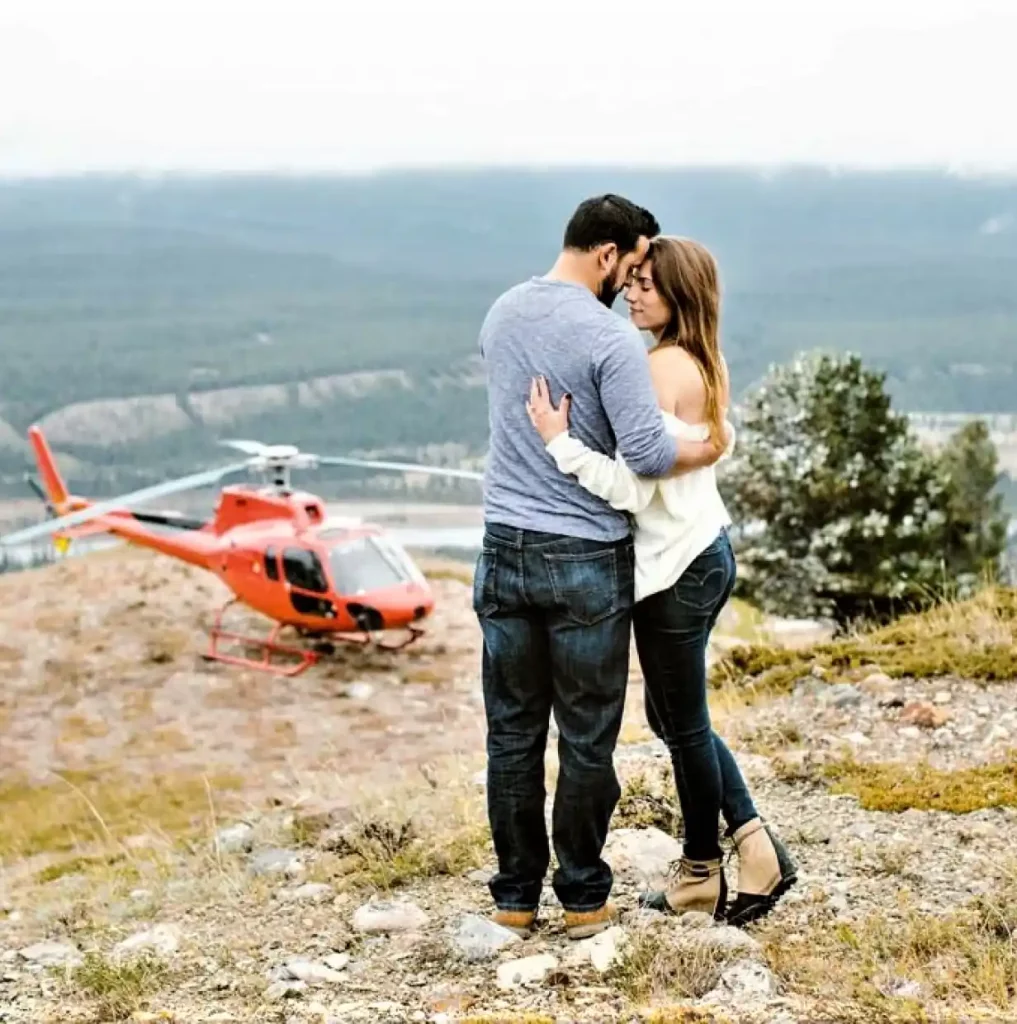 two people hugging on top of a mountain with a helicopter in the background