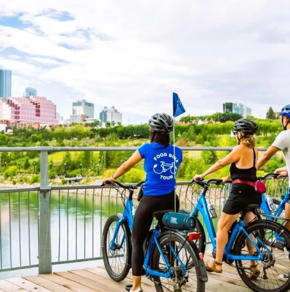 Group of people on bikes one lady's shirt readying Food Bike Tour view of Edmonton city skyline