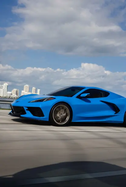 Blue 2024 corvette driving on a highway with city scape in the background